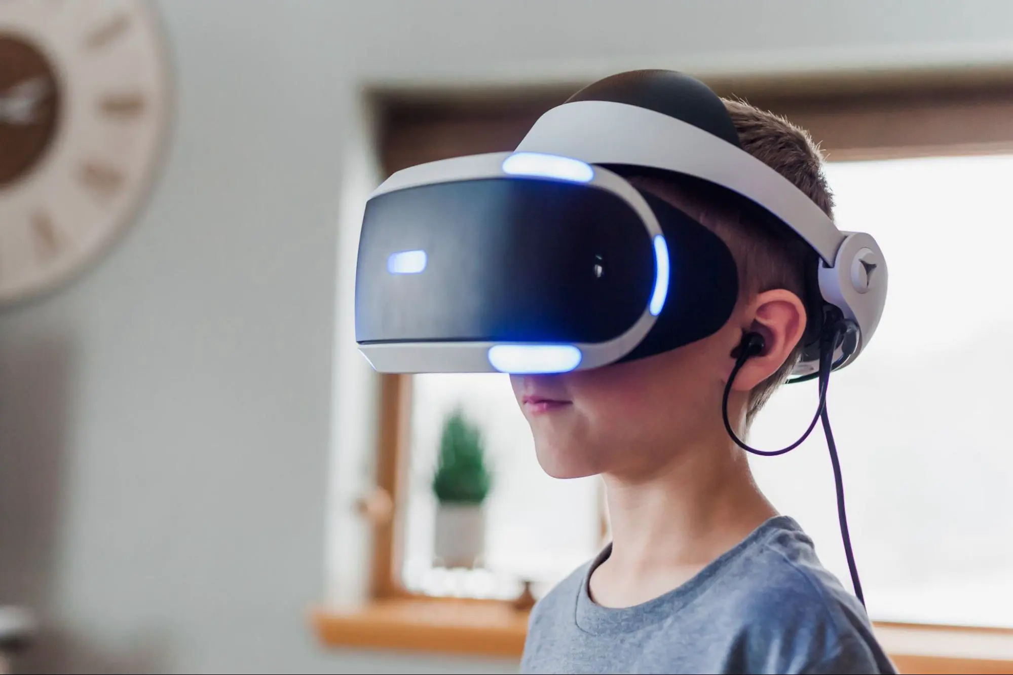 Boy wearing a white PlayStation VR headset with glowing blue light strips, playing at home